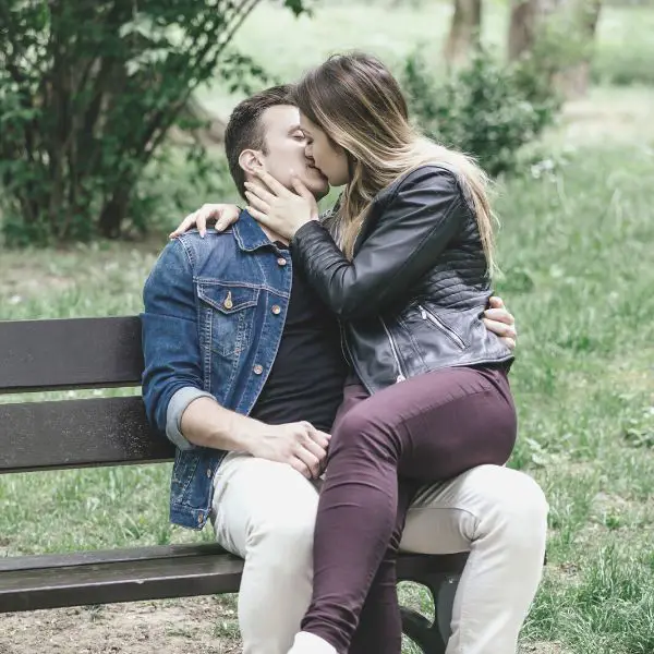 Woman sitting on mans lap in the park kissing him
