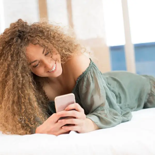 girl laying in bed smiling at a text from guy