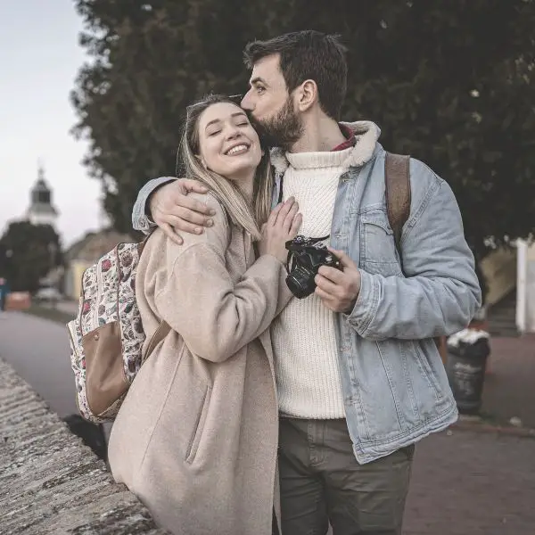 Guy holding a nice camera kissing a smiling girl on temple