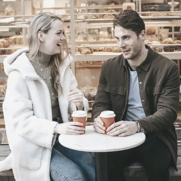 Guy making a girl laugh while drinking coffee in bakery